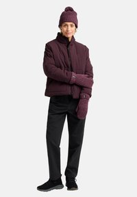 Giacca puffer borgogna con colletto alto, abbinata a un cappello di maglia e muffole coordinati. Pantaloni neri e scarpe scure completano l'outfit.