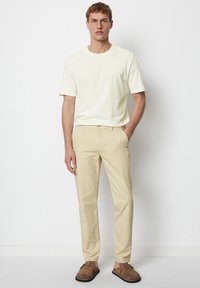 Light beige trousers and a pale yellow crew-neck t-shirt, paired with brown slip-on shoes. Simple design, casual fit, and smooth texture.