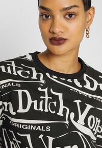 Black T-shirt featuring large white text logos. Short sleeves, round neck, and soft fabric with a casual design. Minimalist accessories visible.