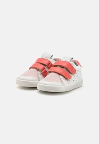 Zapatillas blancas con acentos rosa y correas de gancho y bucle rojas. Materiales de ante y cuero texturizados, diseño bajo y detalles perforados.