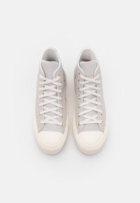 Lichtgrijze hoge sneakers met een gladde textuur, gouden veterogen, witte veters en een beige rubberen neuskap. Bovenaanzicht weergegeven.