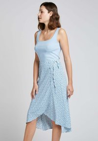 Débardeur bleu clair à encolure carrée associé à une jupe fluide de style portefeuille dans un motif floral bleu clair, avec un ourlet asymétrique.