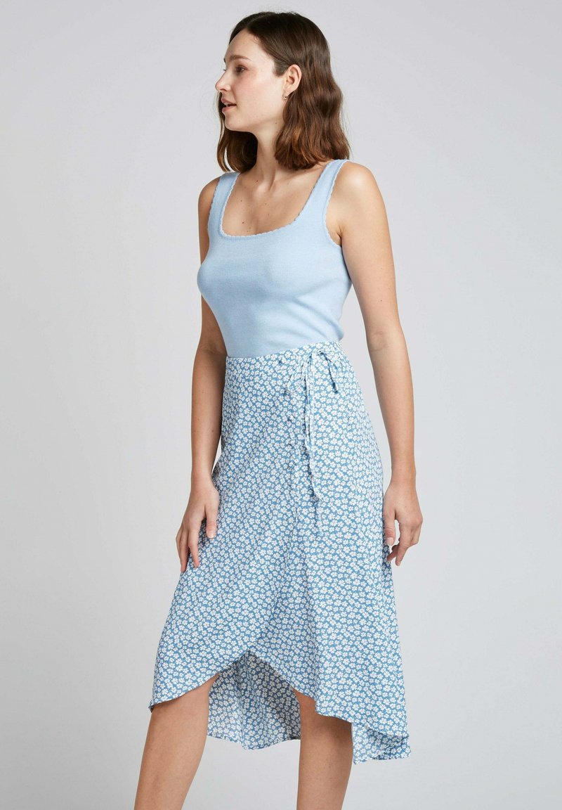 Débardeur bleu clair à encolure carrée associé à une jupe fluide de style portefeuille dans un motif floral bleu clair, avec un ourlet asymétrique.