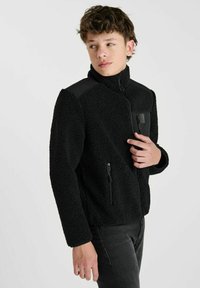 Zwarte fleecejack met een hoge kraag, een ritssluiting aan de voorkant en zijzakken. Het heeft een gladde zwarte schouderaccenten en een gestructureerd lichaam.