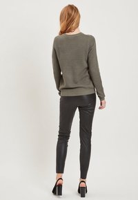 Olivgrön, texturerad tröja ihop med svarta leggings i konstläder. Klädseln inkluderar ankelremsskor med blockklack.