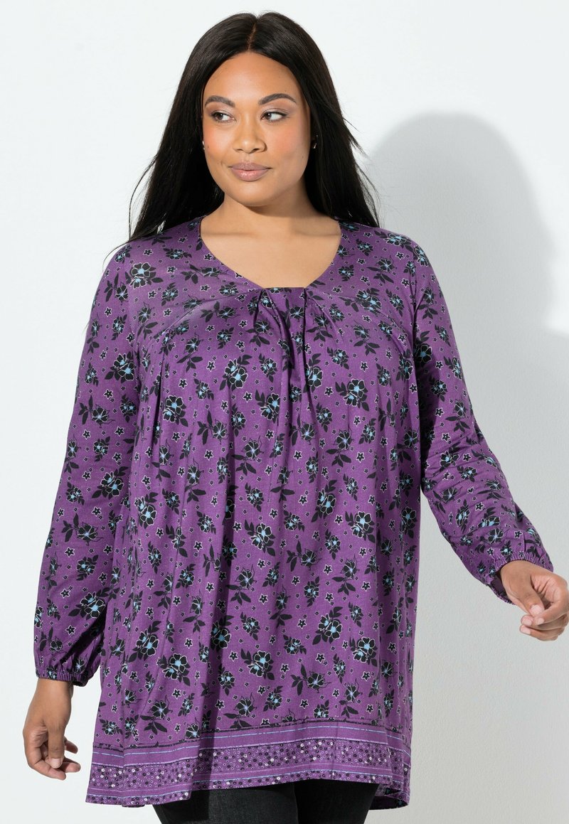 Fioletowa tunika w kwiatowy wzór z dekoltem w serek, długimi rękawami, marszczeniem z przodu i ozdobnym dołem z delikatnymi zdobieniami.
