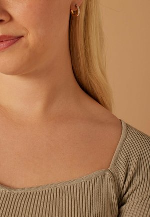 Beige gerippter Top mit quadratischem Ausschnitt, kombiniert mit Creolen: eine aus Gold mit geschwungenem Design und die andere mit kleinen Strasssteinen verziert.