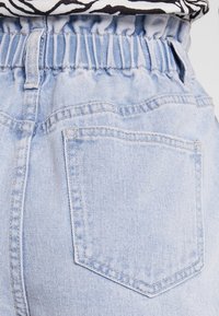 Shorts in denim azzurro chiaro con vita elastica, dotati di una tasca posteriore singola e orlo sfilacciato. Il tessuto appare morbido e leggermente consumato.