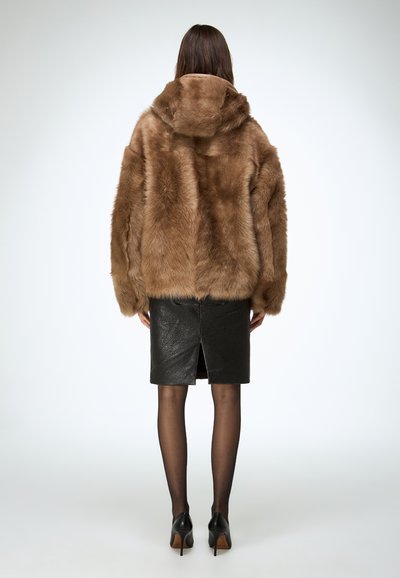 Brown faux fur hooded jacket with a loose fit, paired with a black leather pencil skirt featuring a rear slit. Black stockings and heels.