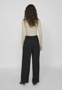 Pantalons larges noirs avec une texture lisse et une taille élastique, associés à un haut beige ajusté à manches longues. Design simple, sans motifs visibles.