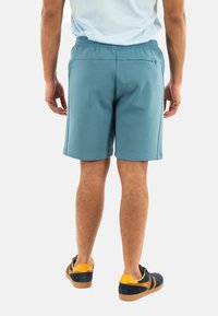 Pantaloni corti sportivi azzurri da uomo con cintura elastica, tasca posteriore, superficie liscia e taglio al ginocchio, abbinati a scarpe casual.