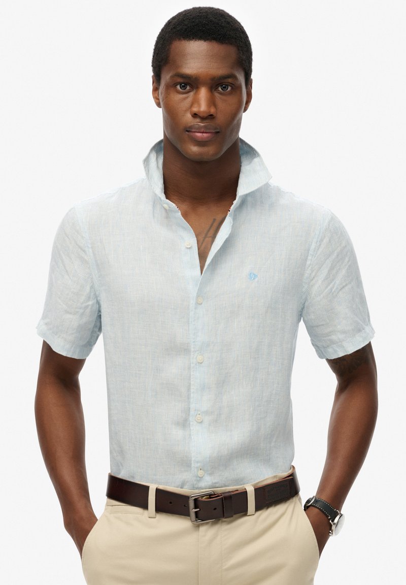 Lichtblauw overhemd met korte mouwen, gemaakt van textuurstof, met een knoopsluiting en een klein geborduurd logo op de borst.