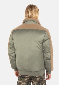Polstret bomberjakke i olivengrøn med beige faux fur-krave og skulderdetaljer, med ribbede маншетter og kant, blød tekstur.