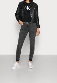 Svart läderjacka, svart grafisk t-shirt, grå smala jeans, rosa och vita sneakers. Slät textur, välsittande design, uppvikta jeansärmar.