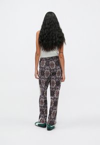 Τα παντελόνια με σχέδιο διαθέτουν έναν συνδυασμό χρωμάτων που περιλαμβάνει μωβ, κόκκινο και γκρι, με ροή σχεδίασης και πλευρικές ρίγες. Συνδυάζονται με πράσινα παπούτσια.