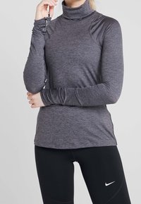 Haut gris à manches longues avec col roulé, coupe ajustée, texture côtelée et fentes latérales ; doté de poignets ajustables avec un détail logo.