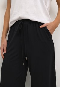 Zwarte loszittende broek met een elastische tailleband en trekkoord. Bevat zijzakken en elegante zilveren hardwareaccenten.