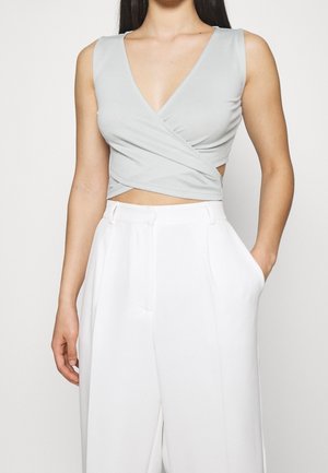 Jasnoszary, bezrękawnikowy crop top z głębokim dekoltem w kształcie V i skrzyżowanym przodem, zestawiony z białymi spodniami o wysokim stanie z bocznymi kieszeniami.