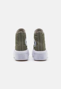 Zapatillas altas de lona verde con suelas de goma blanca, que presentan un parche de logo redondo en el talón exterior y costuras blancas en contraste.