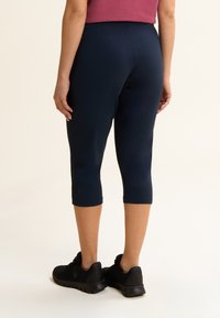 Leggings capri azul marino hechos de material elástico, con un diseño ajustado y una cintura elástica. Usados con zapatos deportivos negros.