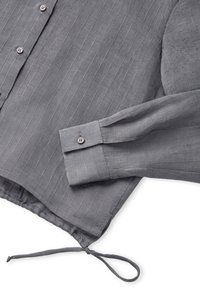 Camicia a strisce grigie realizzata in tessuto leggero con polsini abbottonati. Presenta un orlo con cordino e righe verticali per texture.