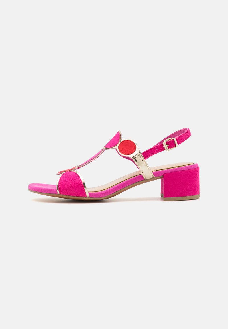 Pink suede sandal with T-strap design, gold accents, and a block heel. Features circular red and pink details on the upper.