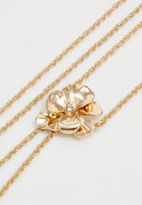 Collar de cadena de oro con un colgante brillante en forma de flor que presenta cinco pétalos y una gema transparente central sobre un fondo blanco.