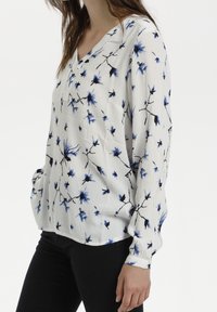 Lettet, langærmet bluse i hvidt stof med et blomstermønster i blå og sort. V-hals-design med en afslappet pasform.