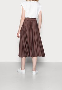 Jupe midi plissée marron avec une taille élastique, associée à une chemise blanche et des chaussures blanches à enfiler. Texture lisse et design fluide.