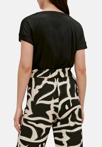 Camicetta nera a maniche corte abbinata a pantaloni beige e neri larghi con motivi astratti e dettagli a pois.