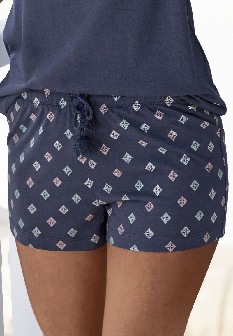 Pantalones cortos azul marino con un patrón de diamantes en rosa claro, menta y blanco. Con cintura elástica y cordón con borlas. Textura de tela suave.