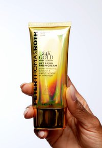 Guldtub med en iriserande yta, svart text och geometrisk design. Innehåller 50 ml av 24K Gold Lift & Firm Prism Cream.
