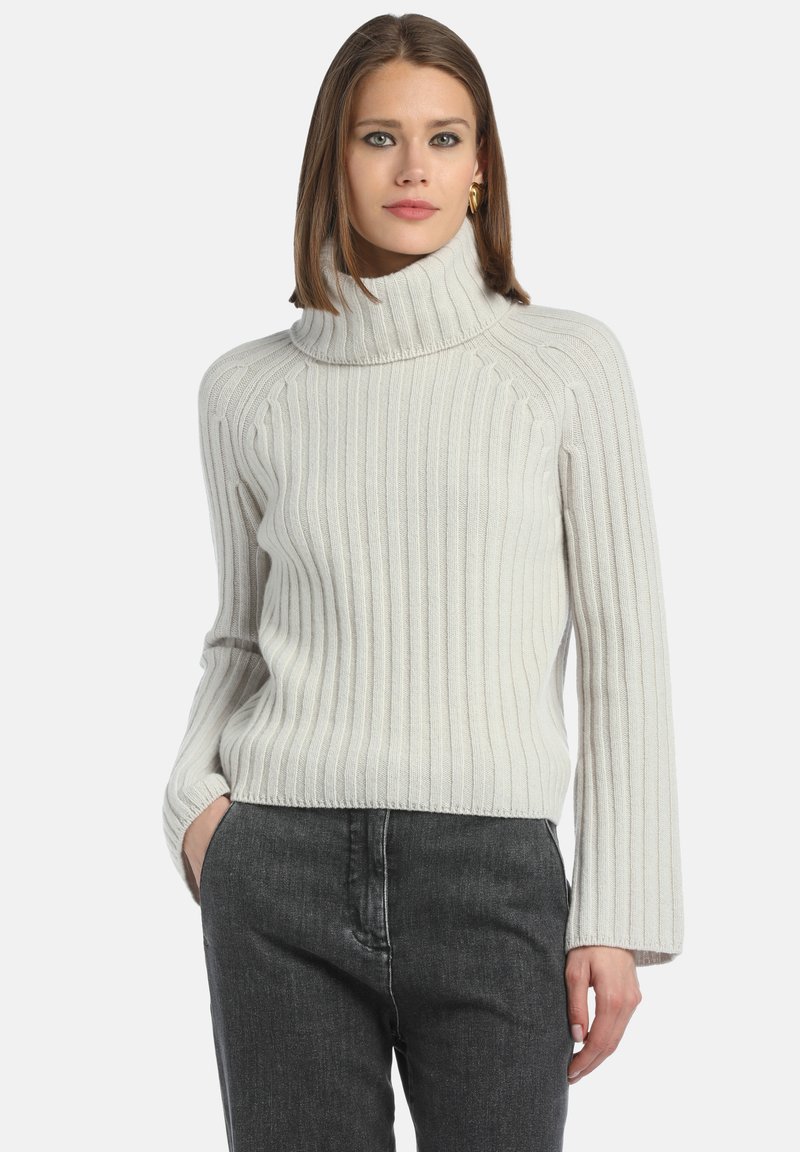 Maglione a collo alto a coste crema con maniche lunghe. Texture morbida e vestibilità rilassata. Abbinato a jeans grigio scuro.