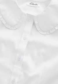 Weißes Hemd mit Rüschkragen und fünf Knöpfen auf der Vorderseite. Das Material wirkt glatt und ist knitterfrei, mit einem Etikett "Clarks".
