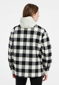 Gequilted geruite jas met zwart, wit en grijs geblokte patronen, een witte capuchon en geribbelde manchetten, met een relaxte pasvorm en een royale snit.