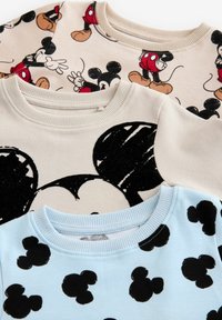 Trois sweat-shirts superposés : beige avec des graphiques rouge et noir de Mickey Mouse, beige avec un grand visage noir de Mickey, bleu clair avec des silhouettes noires de Mickey.
