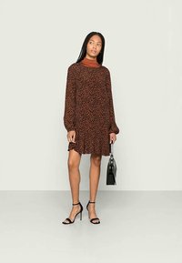 Vestido com padrão de leopardo castanho, de mangas longas, ajuste relaxado e bainha franzida. Combinado com saltos pretos com tiras e uma bolsa preta.