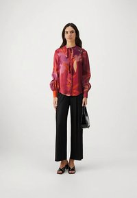 Värvikas, mustriga lahtise lõikega pluus kaelakaeluse ja nööriga, pikkade puffvarrukatega ning nööpidega esiküljel; kombineeritud mustade volditud pükste ja sandaalidega.