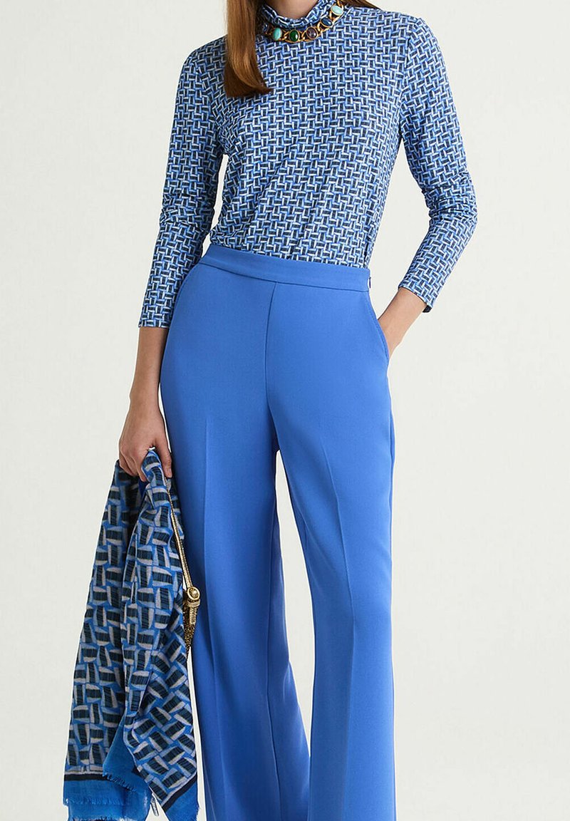 Pantalon bleu ajusté assorti à un haut bleu à manches longues à motifs. Le haut présente un design géométrique et un col montant, orné d'un col en perles colorées.
