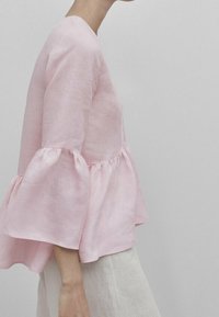 Haut en lin rose avec un design de manches évasées et volantes, présentant un col rond et une coupe ample et décontractée. Texture lisse, tissu léger.