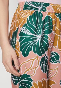 Πολύχρωμο λουλουδάτο παντελόνι από σατέν ύφασμα. Διαθέτει μεγάλους πράσινους και ροζ λουλουδάτους σχεδιασμούς σε ροδαλό φόντο, με ελαστική μέση.