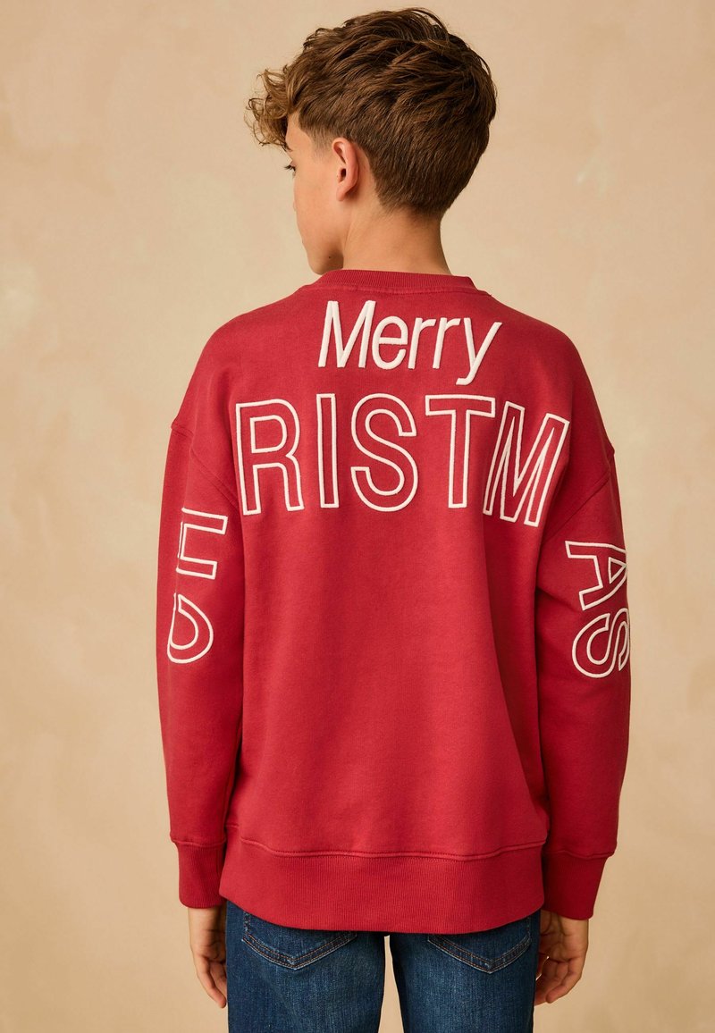 Sweatshirt rouge en mélange de coton, avec le texte brodé en blanc "Joyeux Noël" dans le dos. Coupe décontractée avec des poignets côtelés.