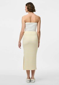 Een strapless witte top en een aansluitende rok tot de knie met horizontale gele en witte strepen, voorzien van een zijsplit tot aan de zoom.