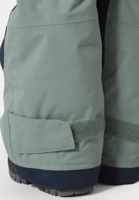 Waterdichte sneeuwbroek in lichtgroen met een marineblauwe onderkant. Kenmerken zijn een klittenbandsluiting en een textuur die zorgt voor duurzaamheid.
