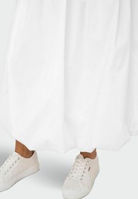 Vit, voluminös kjol med en texturerad yta, kombinerad med ljusa sneakers med snörning och subtila mönster.