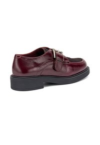 Zapato de cuero burdeos con puntera redonda, detalle de hebilla lateral y suela de goma negra; presenta una zona de empeine texturizada.