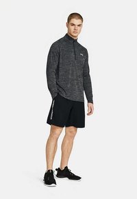 Dark gray long-sleeve shirt with a half-zip neck, paired with black shorts featuring white text. Black athletic shoes complete the outfit.