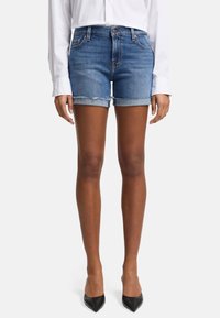 Shorts en denim bleu clair avec un ourlet effiloché et des revers roulés. Associés à une chemise blanche à manches longues et des escarpins noirs à bout pointu.