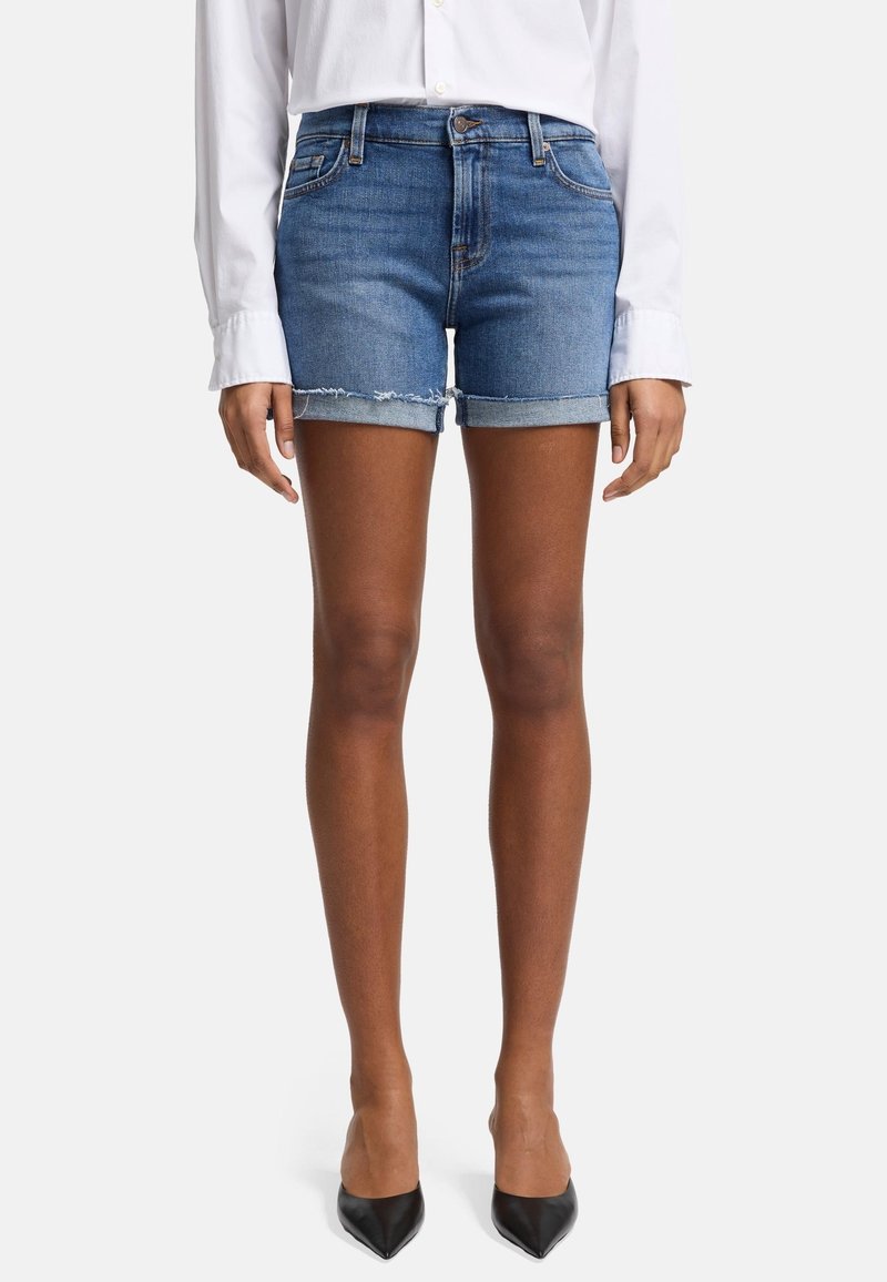 Shorts en denim bleu clair avec un ourlet effiloché et des revers roulés. Associés à une chemise blanche à manches longues et des escarpins noirs à bout pointu.