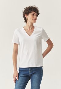 Camiseta blanca de cuello en V hecha de una tela suave, con mangas cortas, combinada con jeans de mezclilla azul. Diseño simple y recto, sin embellishments.